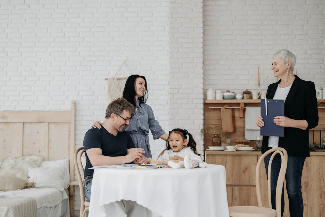 why-choose-us A happy family sits at a table with a child and social worker indoors, symbolizing adoption or foster care.