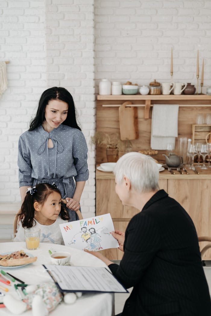 A girl shows her family drawing to two adults in a cozy kitchen, symbolizing love and togetherness.